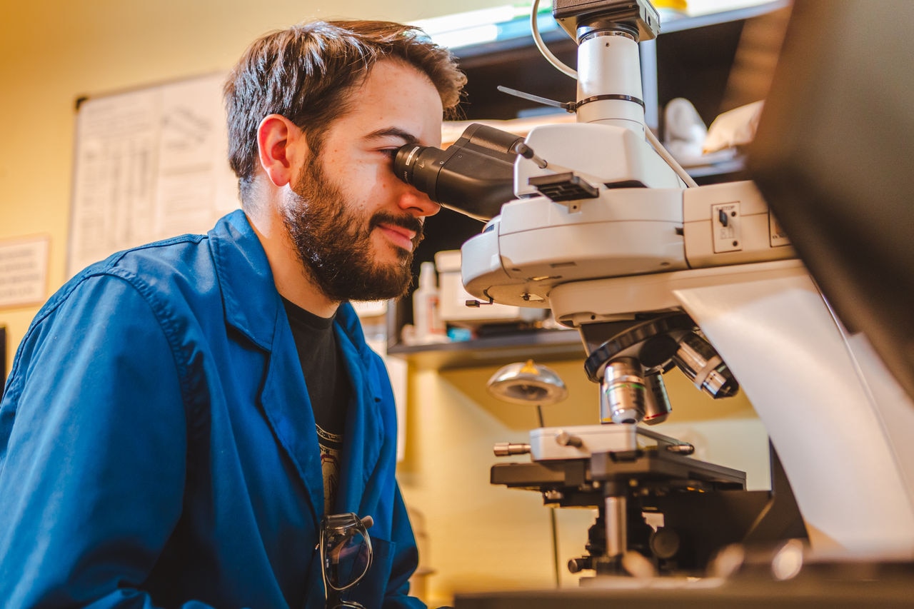 Employee examining a substance under a microscope at BahÃ­a Blanca facility